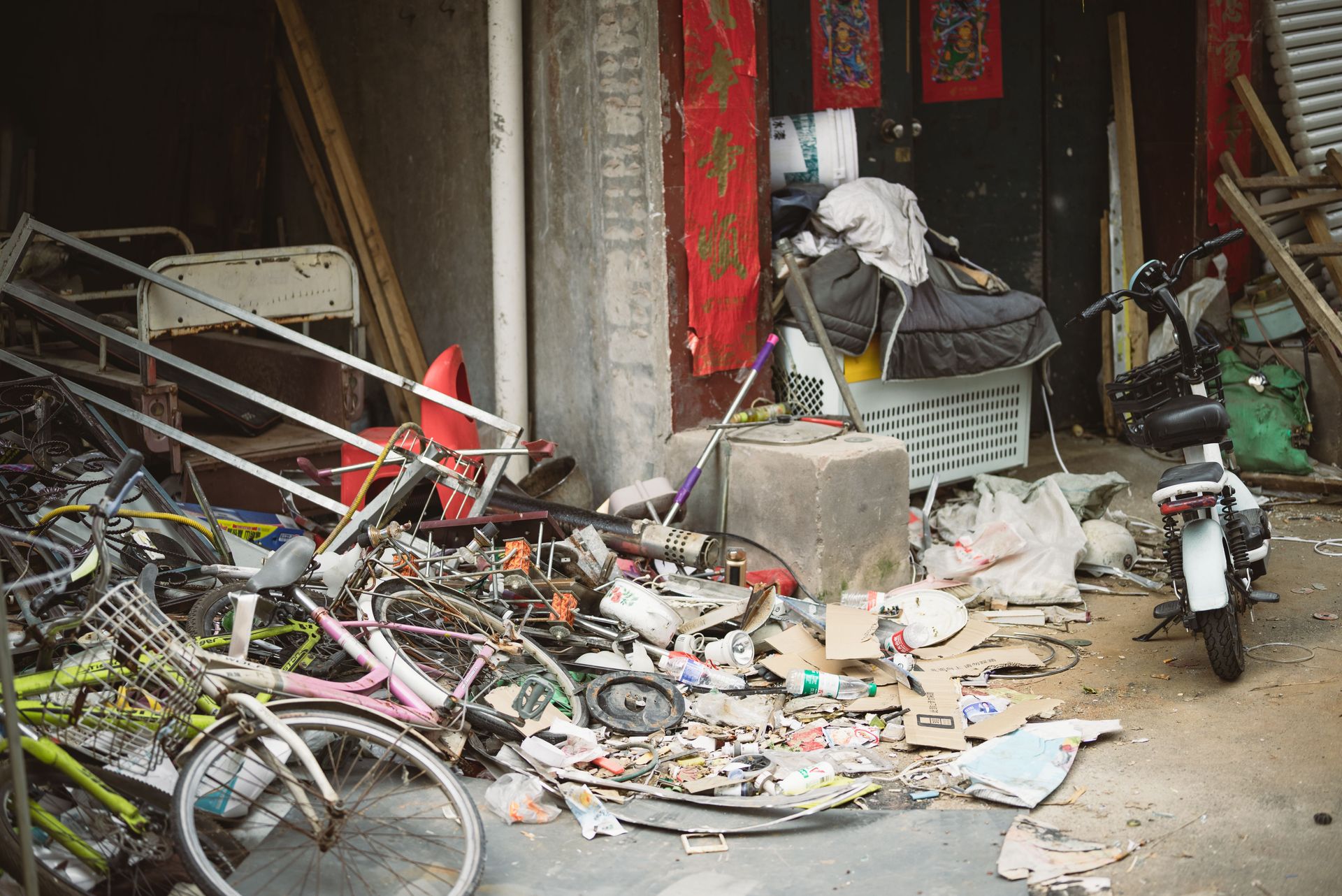 A cluttered alley filled with old bicycles, scrap metal, and miscellaneous debris beside a building.